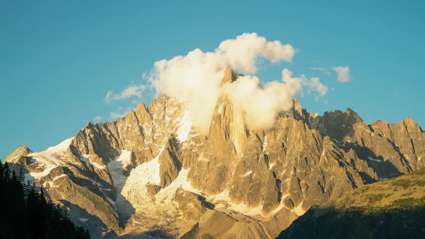 Clouds gather and pass above a tall frozen mountain top