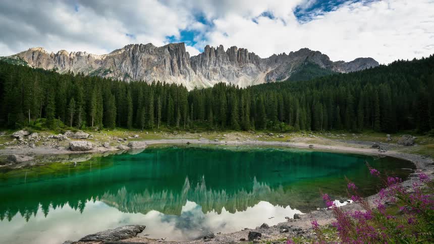 A perfectly still green lake surrounded by trees and mountains