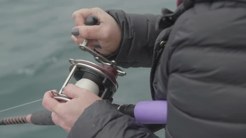 A woman is reeling in her fishing line outside during the day