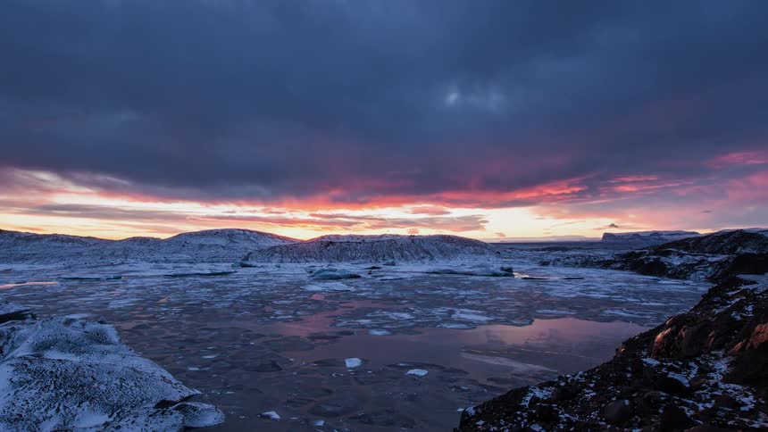 Time lapse of the sun setting over a body of water with chunks of ice in it