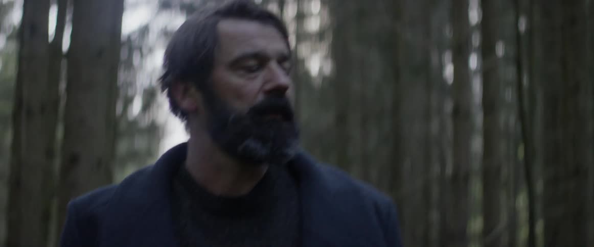 A man is walking in the woods and appears sad and worried