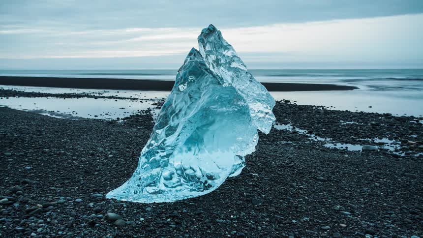 An iceberg is sitting on a beach melting during the day