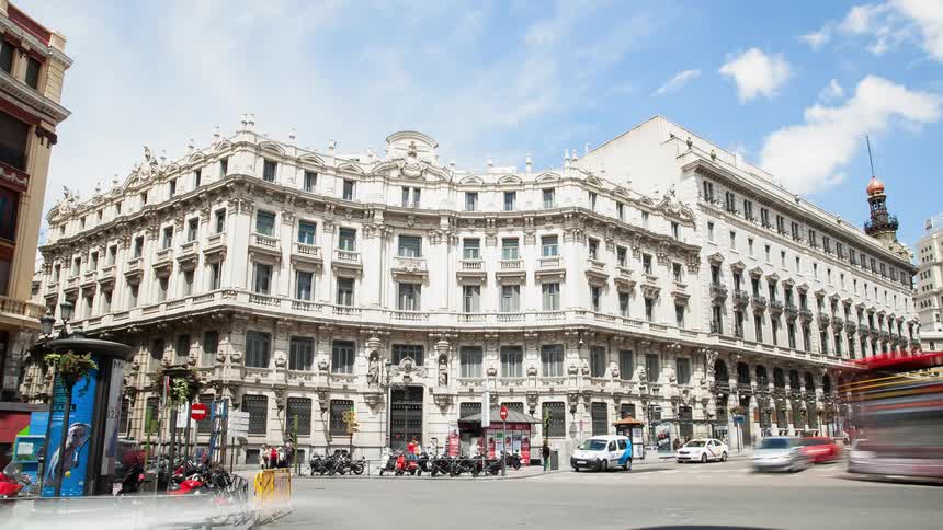 Cars driving down a street and people walking on a sidewalk next to a large white building