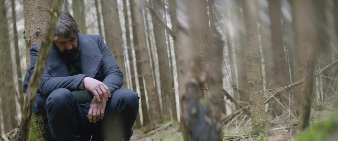 Man slumps against a tree in a forest