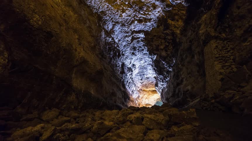 A light dimly illuminates the end of a cavern