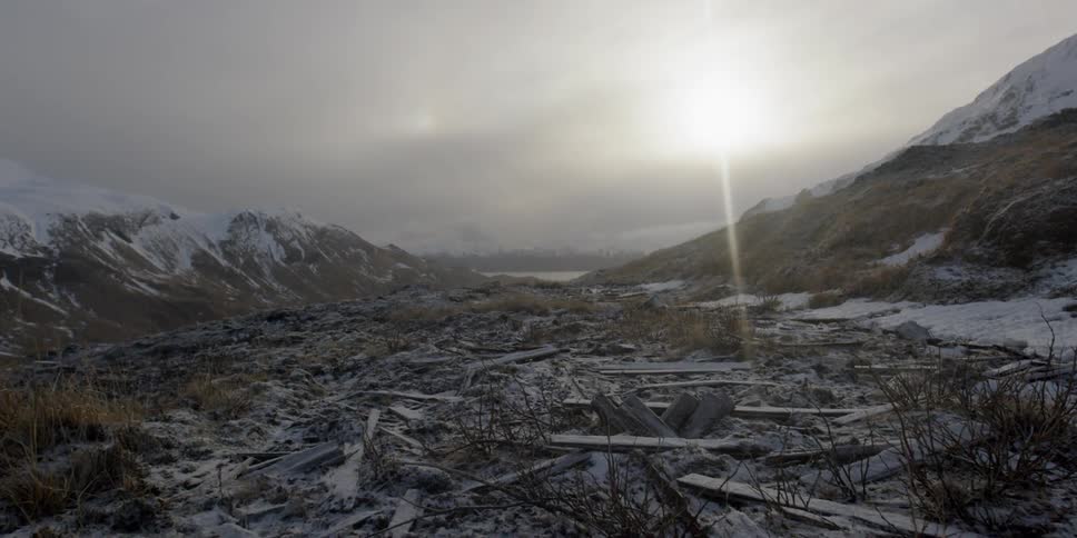 The sun shines through the clouds on a clearing with planks and debris