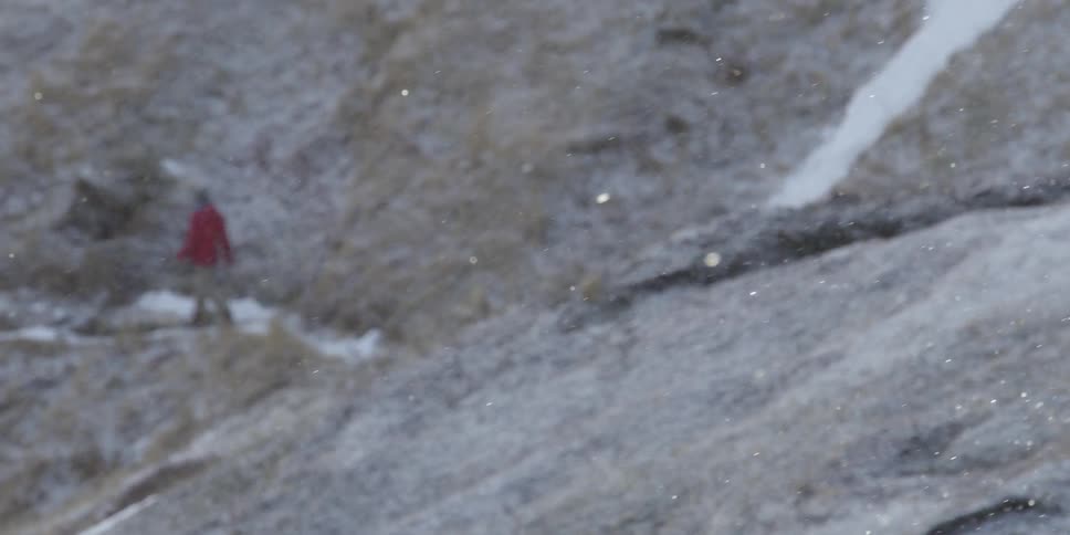 A hiker walks a trail on a mountain slope as snow falls