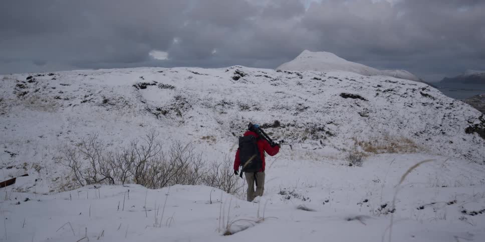 A man walks on the snow covered field carrying a tripod