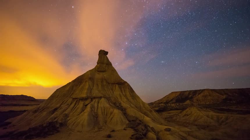 Clouds float over a rock formation in a desert