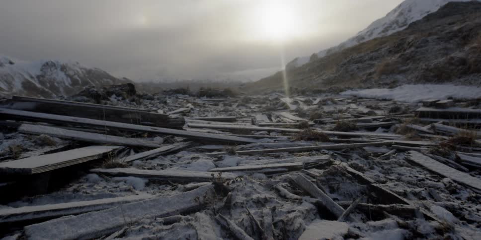 Snow falls gently onto a large mess of boards in a field
