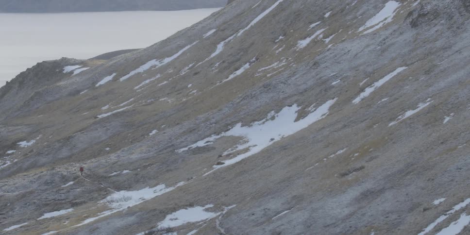 Patches of snow cover a mountainside as a hiker walks