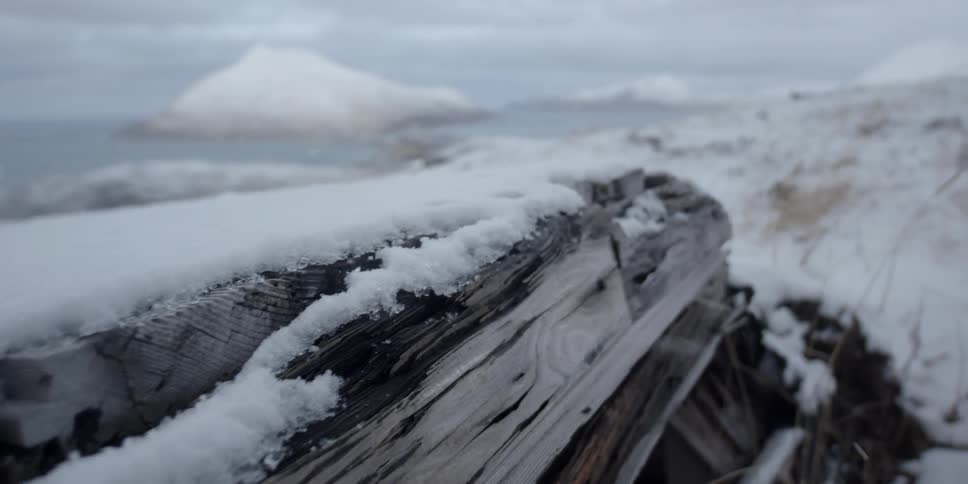 A snow covered piece of wood sits atop a snow covered hill overlooking a body of water