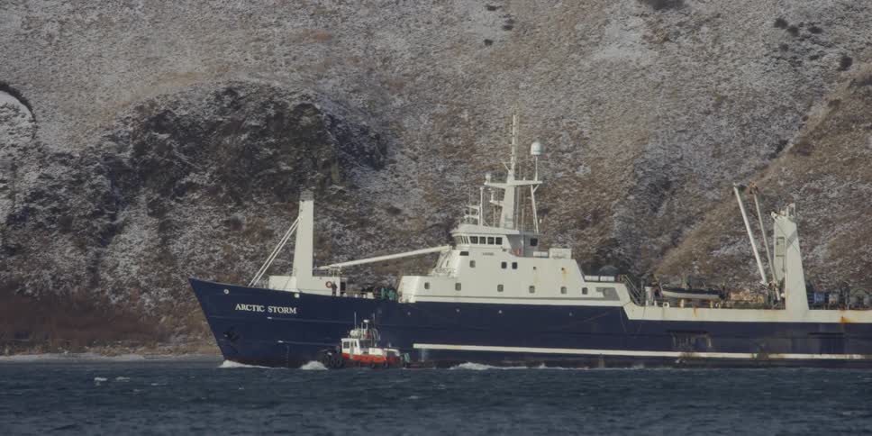 A ship sails past a small tugboat