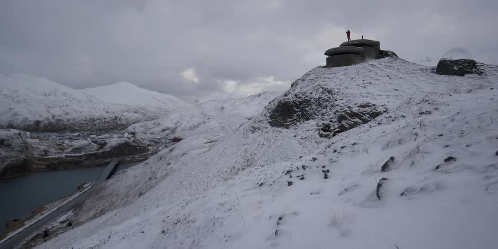 A man stands atop a concrete lookout building in the snow