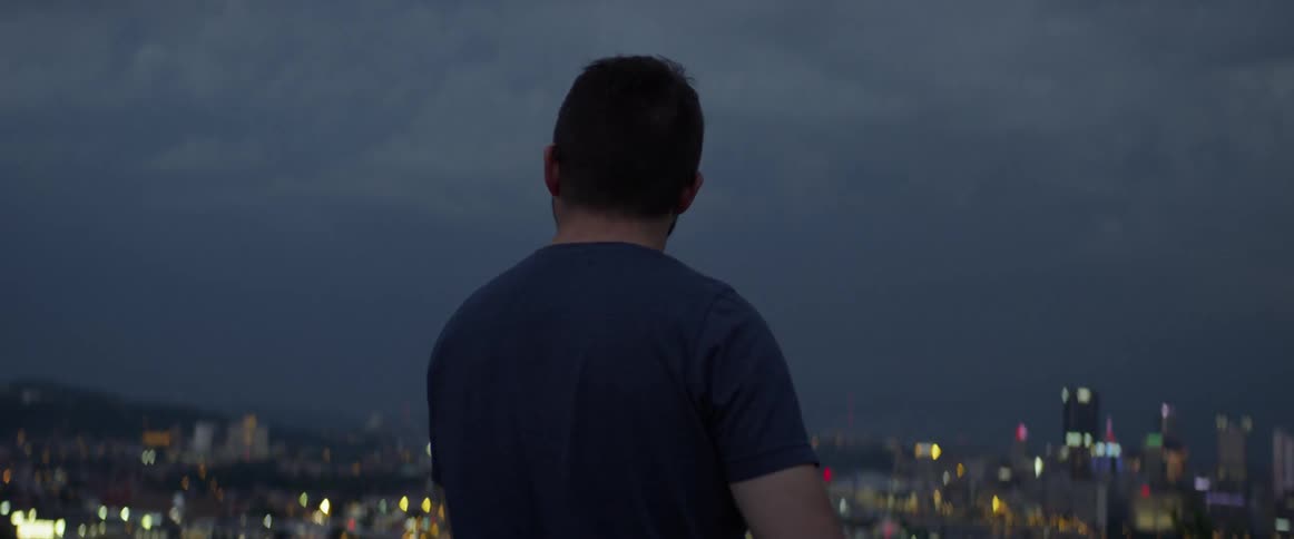 A man watches a lightning storm over the city below