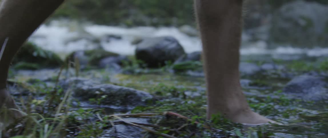 A man walks barefoot through a stream