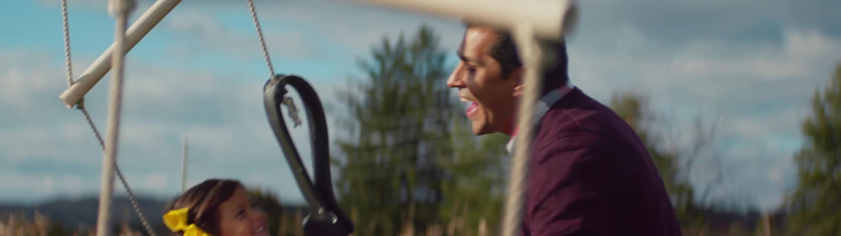 A father is pushing his daughter on a swing