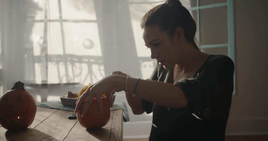 A woman is sitting in her home carving pumpkins during the day