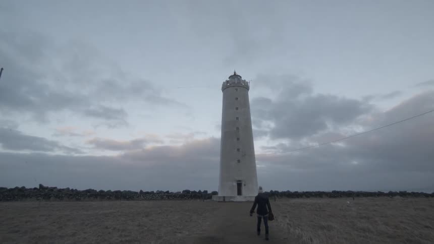 A woman walks a path toward a lighthouse