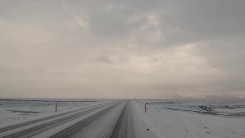 Vehicles driving down a snowy country road on a cloudy day