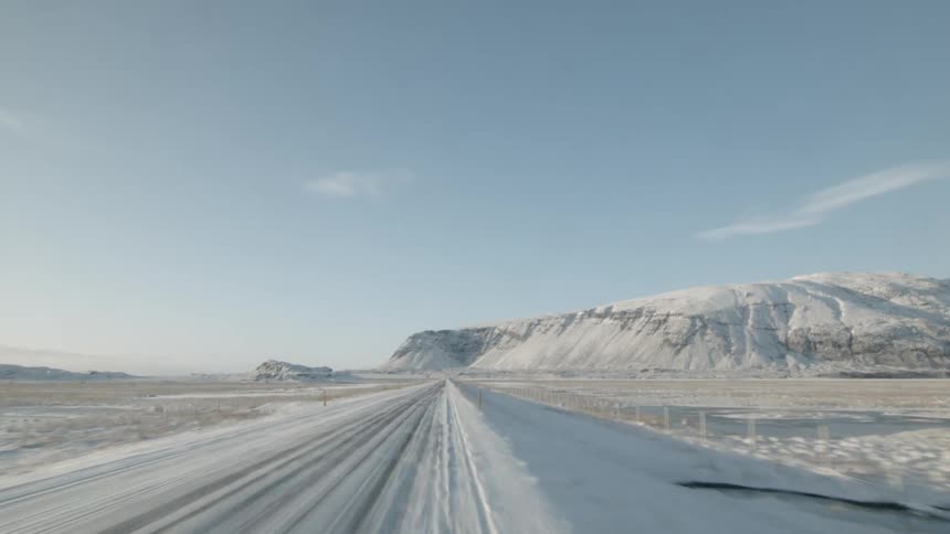 A vehicle drives on a snowy road near mountains