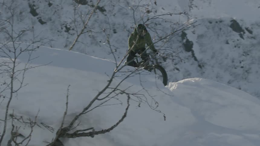 A man rides a bicycle through the snow
