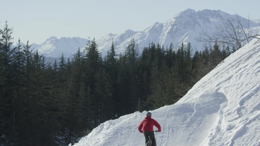 A bicyclist goes over a jump on a snowy mountainside