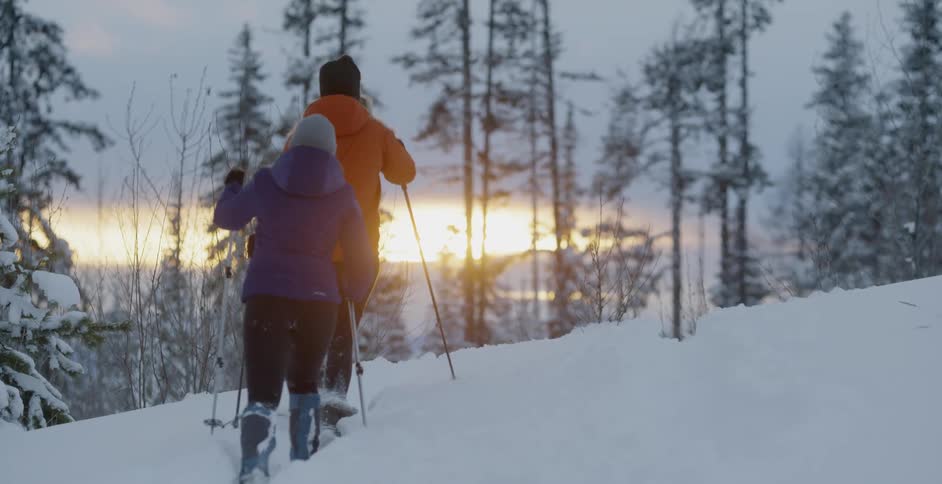 Two people hike in the snow at sunset