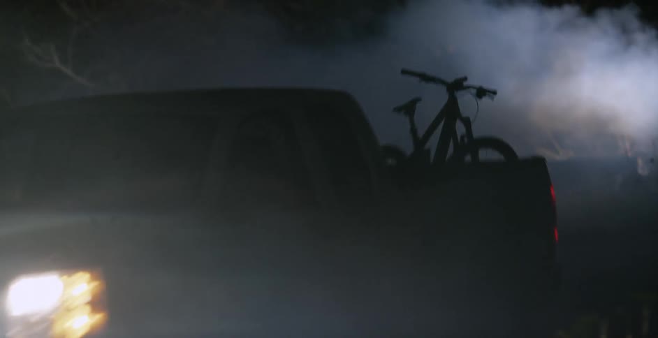 A pickup truck is driving on a foggy road at night