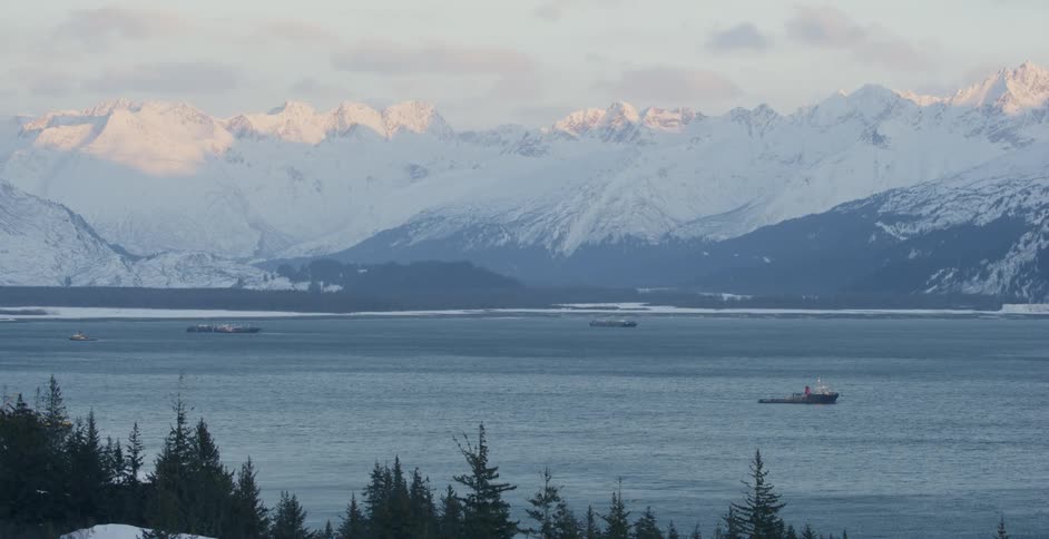 Boats are floating in the ocean off a mountainous coastline in winter