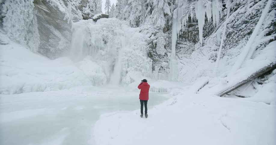 A man is taking photographs of a waterfall falling into a frozen river on a winter's day