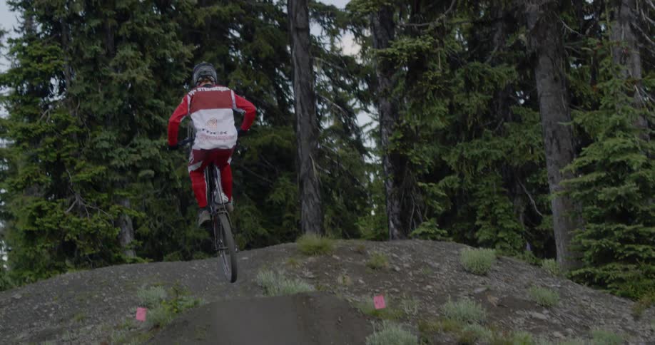 A man is riding a mountain bike up a hill and performing a stunt