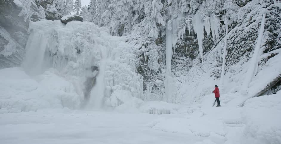 A hiker takes a photograph of an icy waterfall