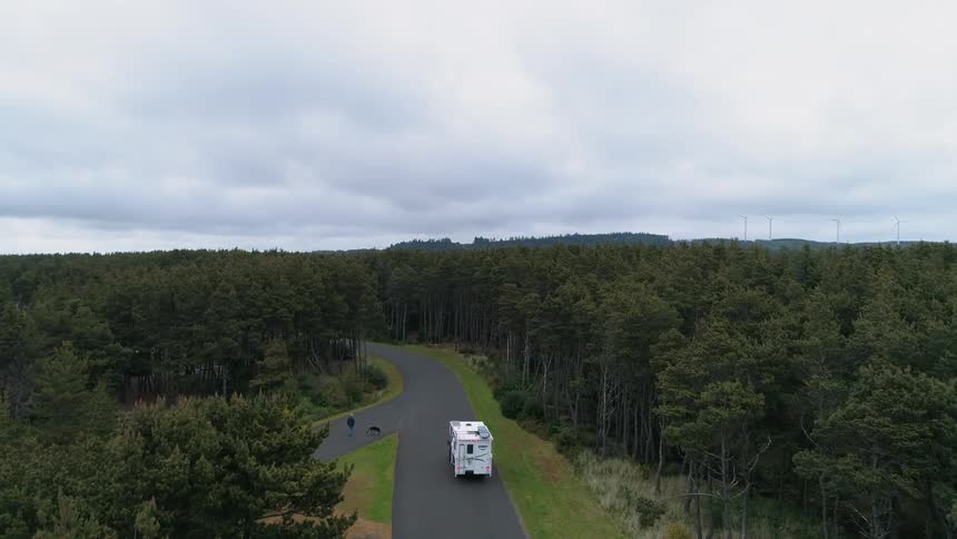 An rv travels along a forest road passing people walking dogs