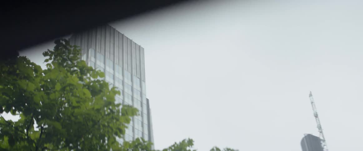A car drives by skyscrapers and trees