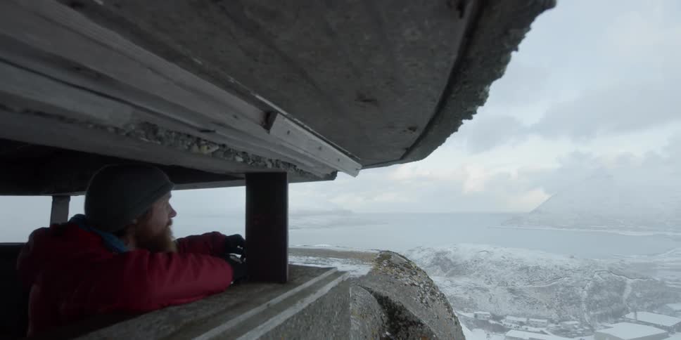 Man looking out from a bunker type structure above town and ocean