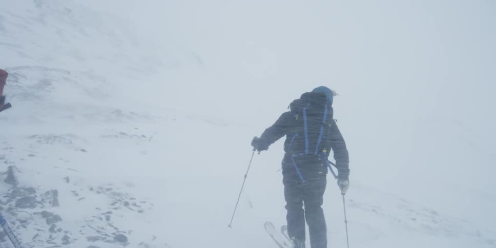 People skiing on the side of a snowy hill on a very windy day