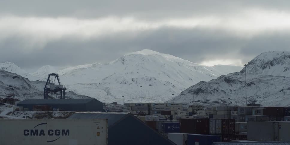 Clouds float over snowy mountains and shipping containers