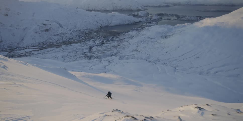 A person wearing a backpack skis down a slope