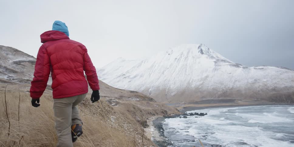 A hiker walks near a snowy shore