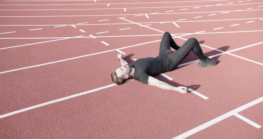 A man lays flat and exhales on a running track