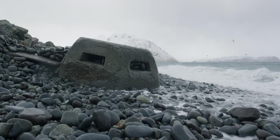A concrete bunker sits on a pebbly beach