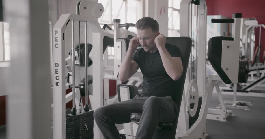 A man is putting earbuds in his ears before working out on some gym equipment