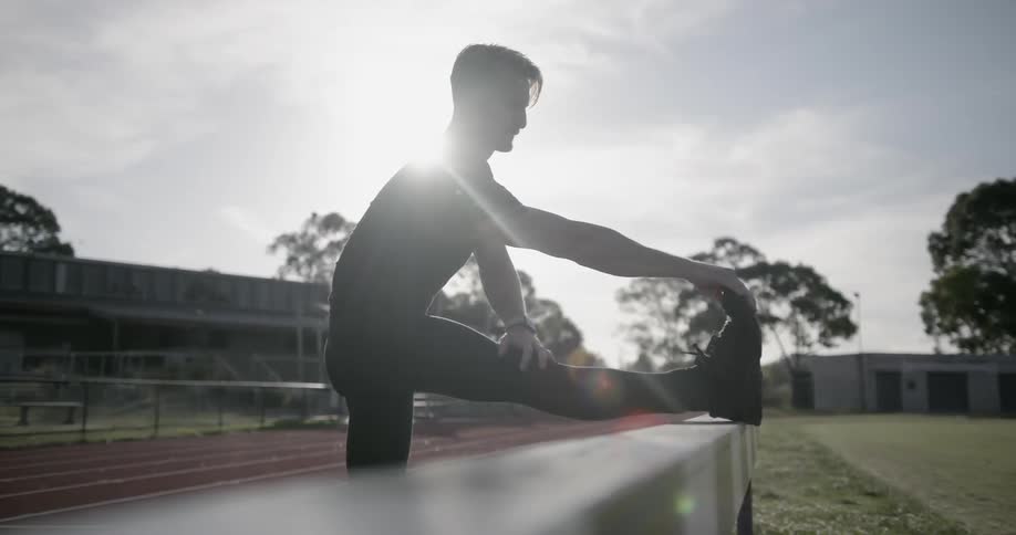 A man stretches on the railing of a running track