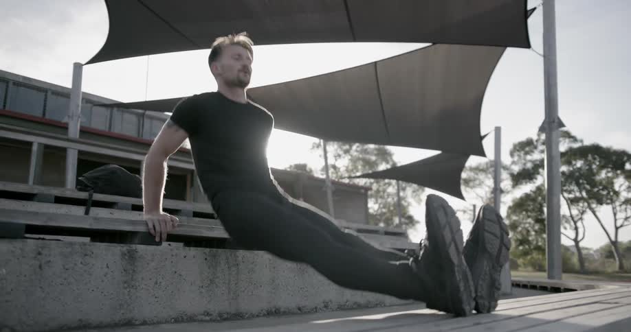 A man does push-ups on outdoor bleachers