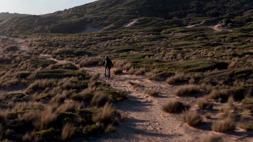 A bicyclist rides along an ocean coast at sunset