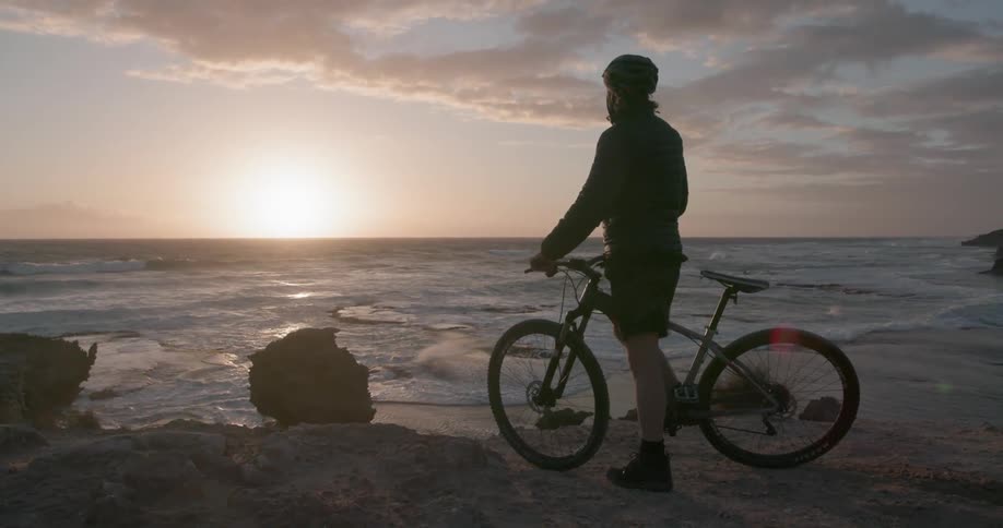 A person bikes toward the ocean and cheers