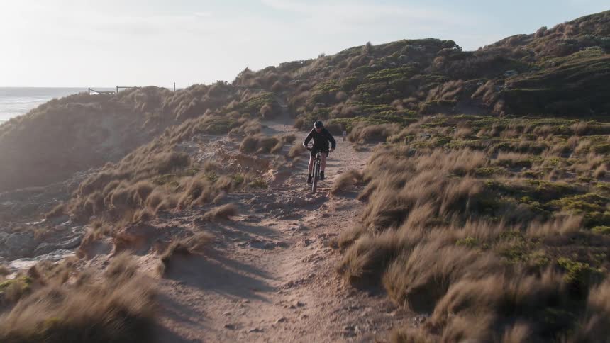 A bicyclist rides along a coast at sunset