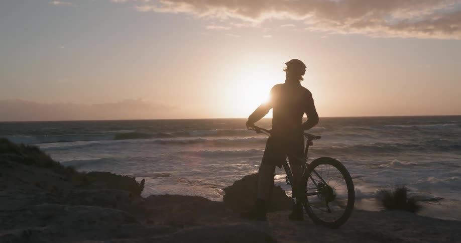 A bicyclist throws his hands up and celebrates looking out over the water