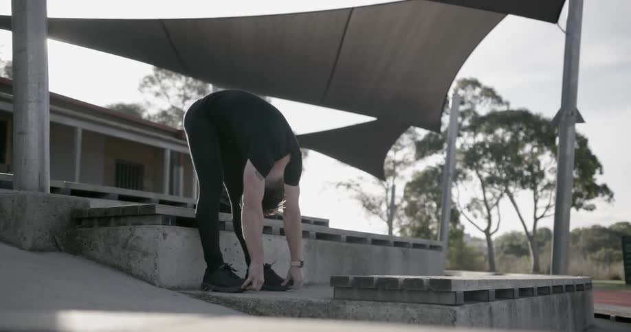 A man is bending over stretching and touching his toes outside during the day